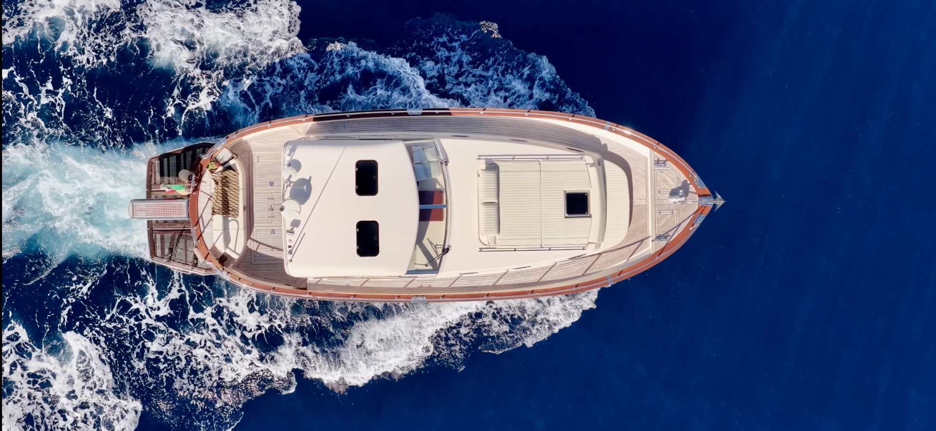 Aerial top view of a boat cruising on deep blue sea with a wake