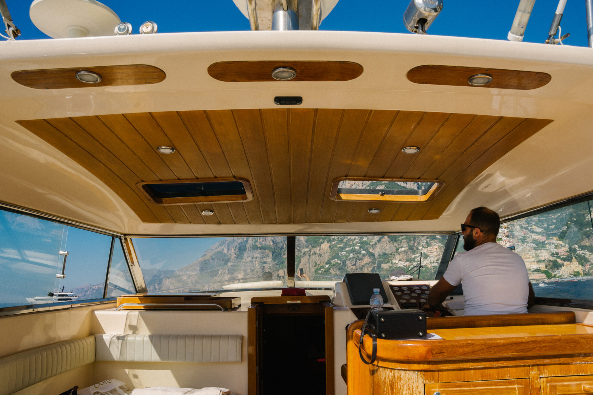 Captain steering the boat from the helm with coastal cliffs in the distance