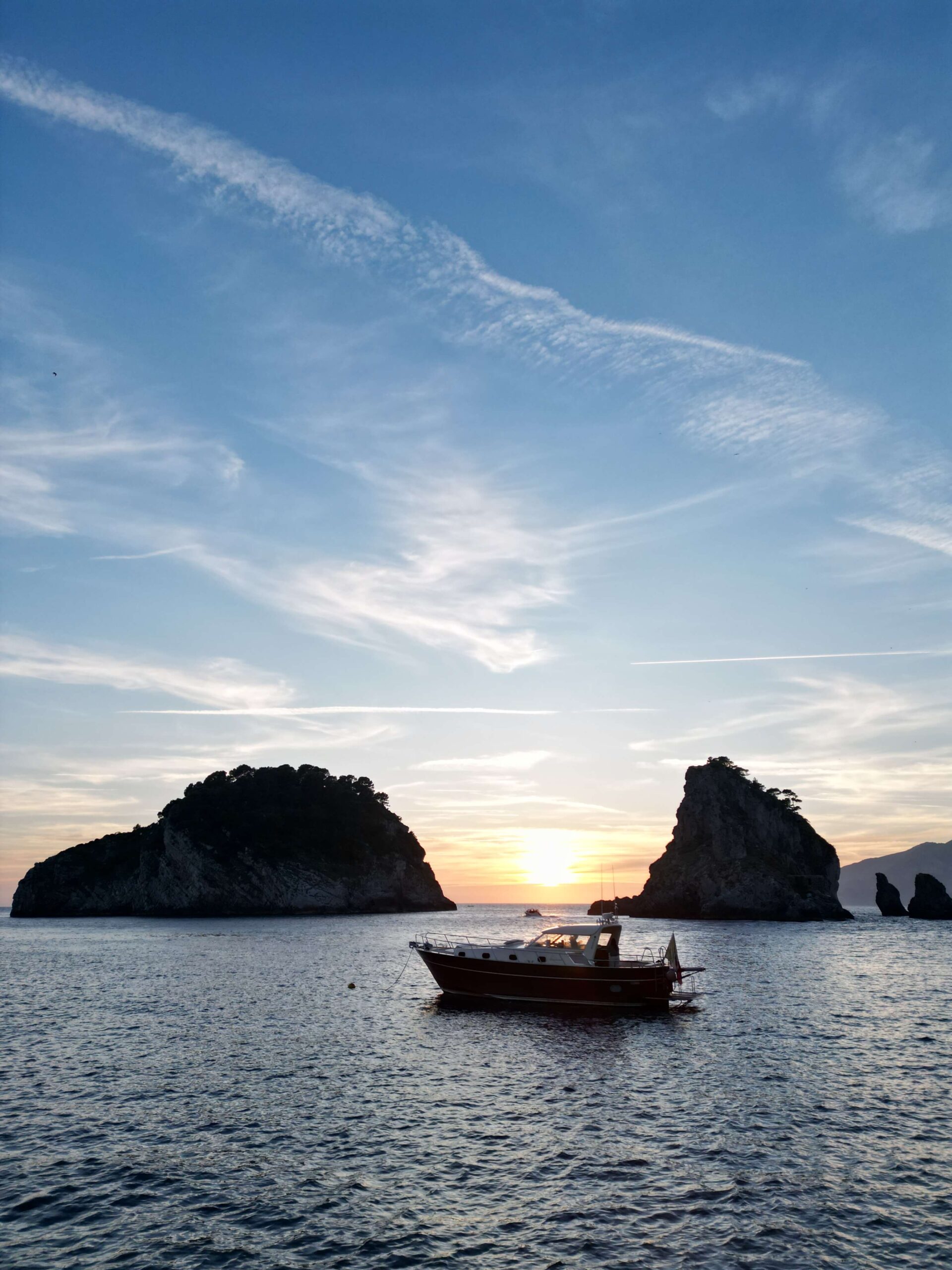 Boat at sea at sunset with rocky islets in the background