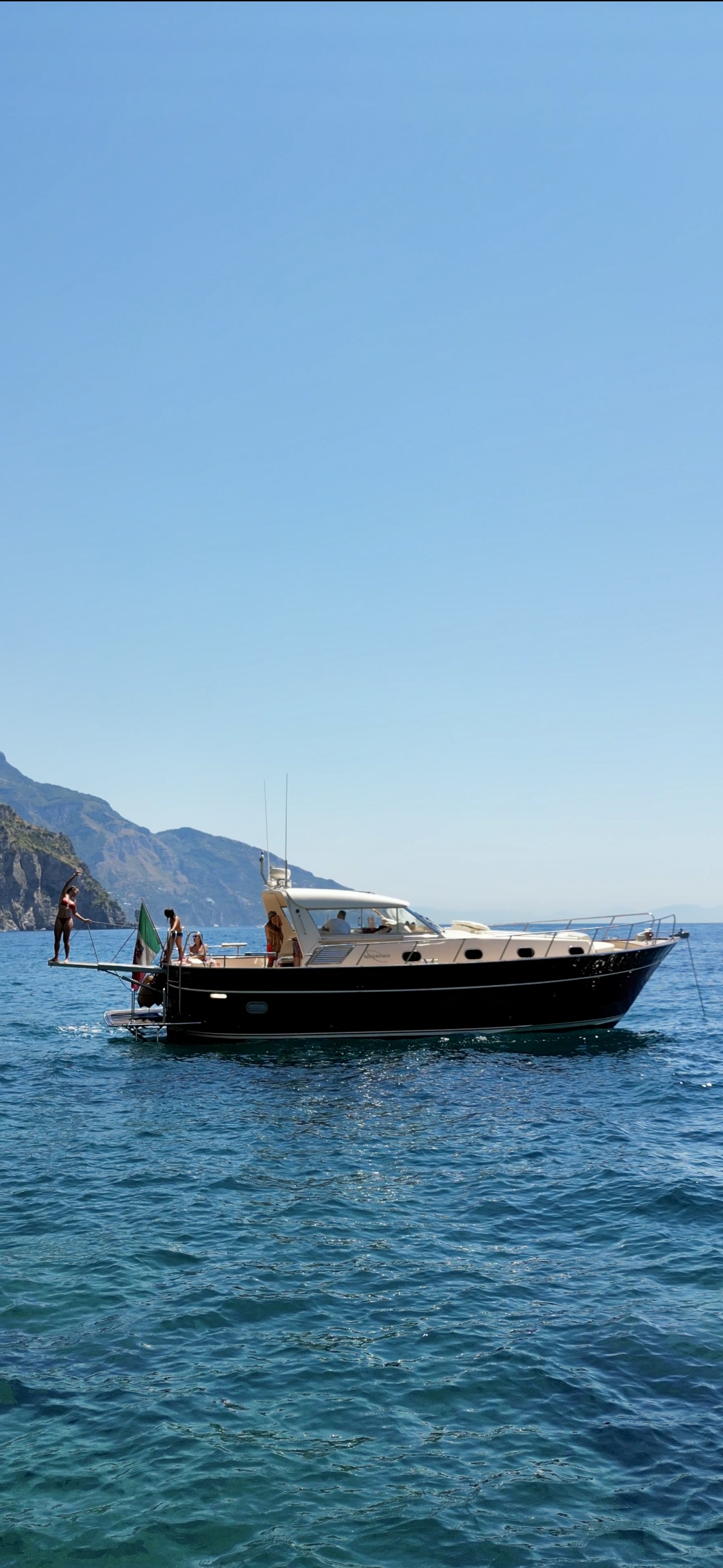 Apreamare 45 gozzo boat off Positano on the Amalfi Coast, with guests on deck and clear blue sea under a sunny sky.