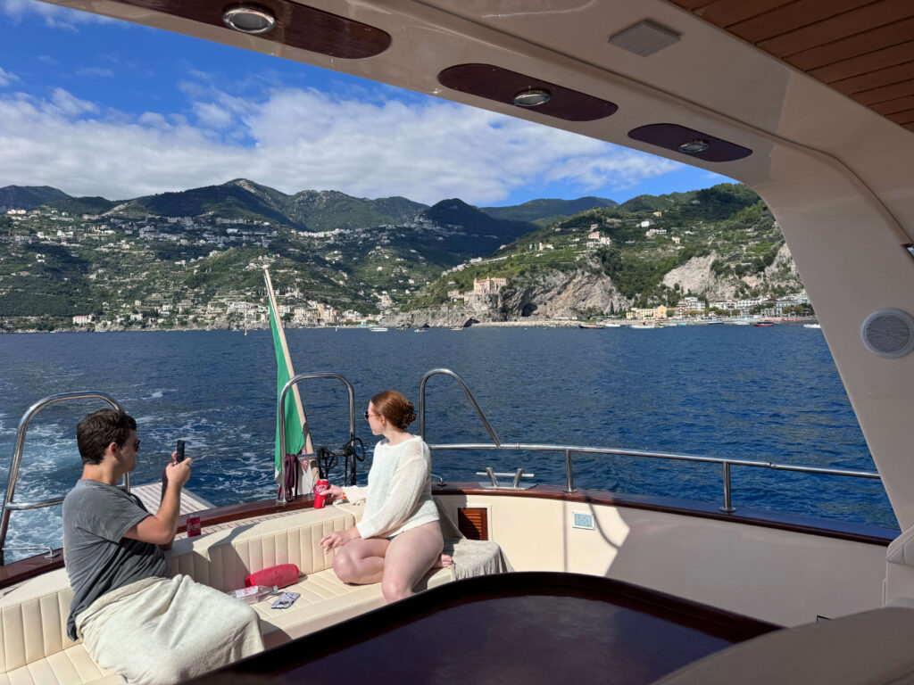 Two people relaxing on a boat lounge with the Amalfi Coast in the background