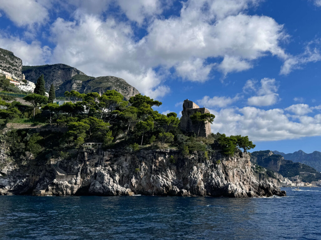 Rocky coastline with pine trees and a stone tower seen from the sea