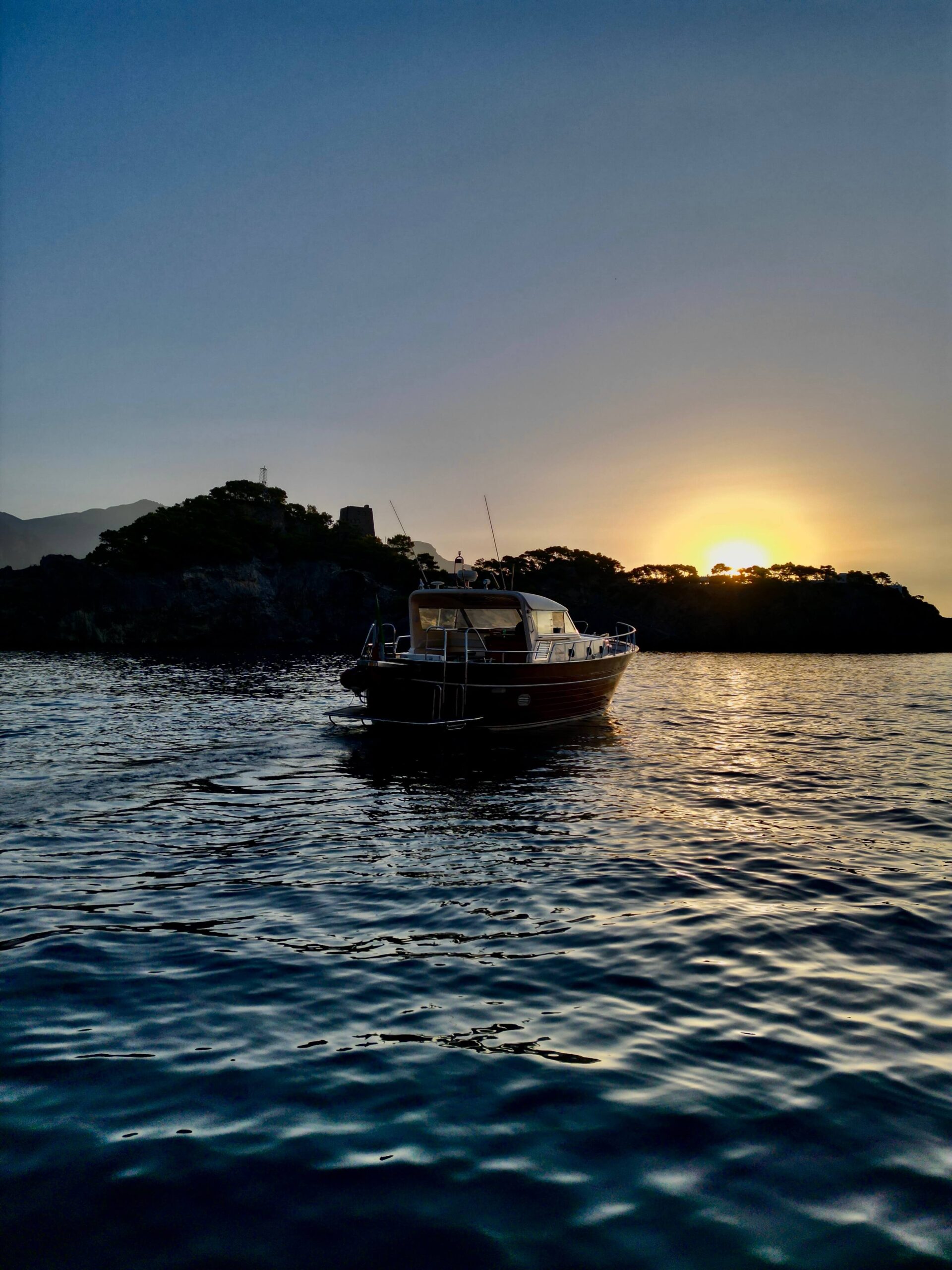Boat at sunset near Li Galli and Nerano with the coastline in silhouette