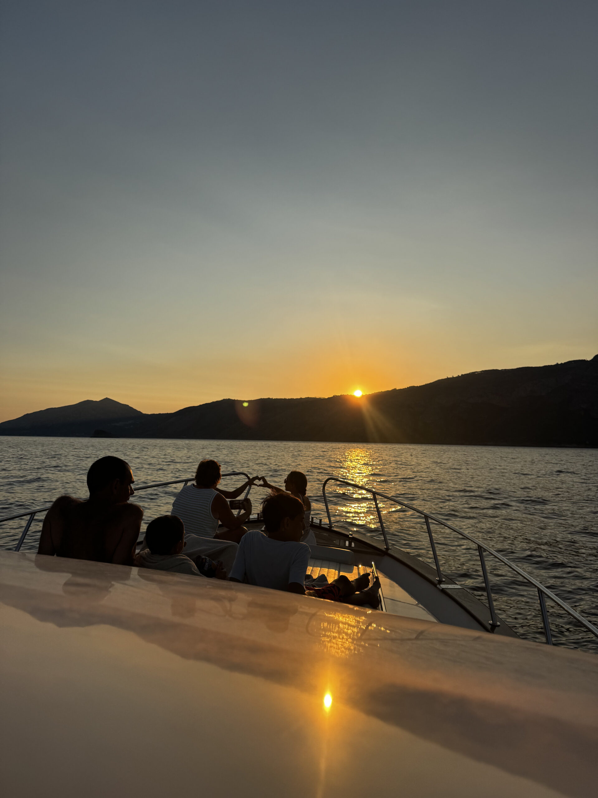People relaxing on the bow during a sunset tour with the sun setting over the water